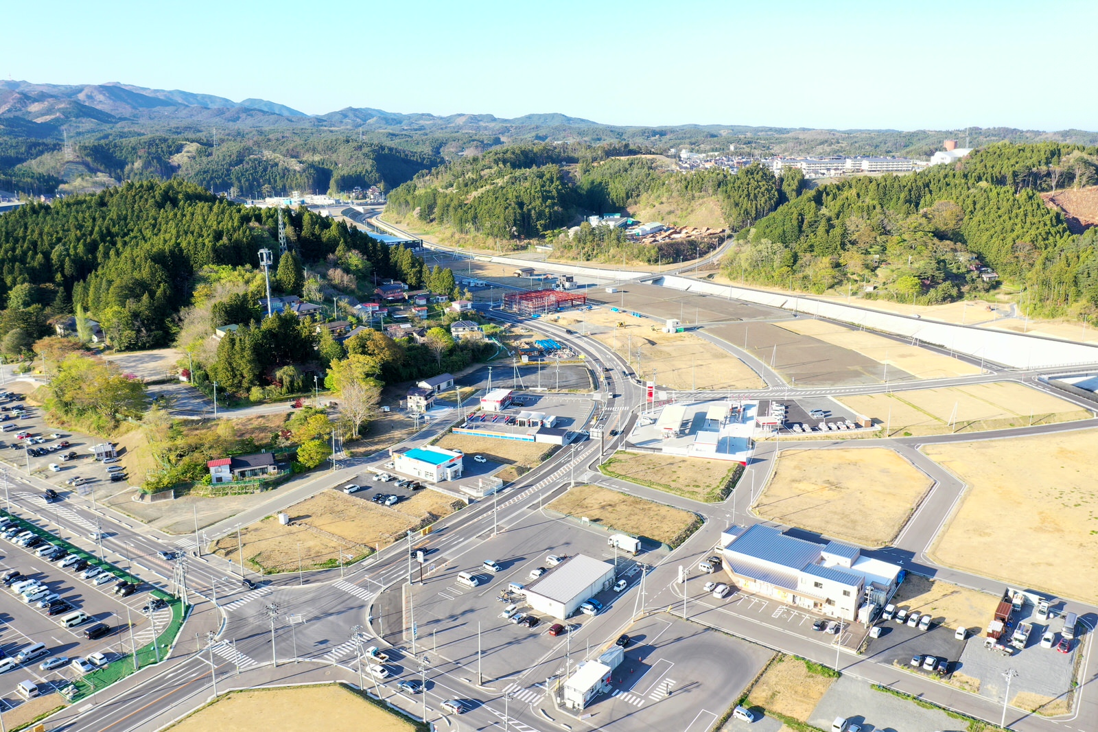 山に囲まれた田舎の町を空から撮影しており、住宅や道路が点在し、自然に囲まれた静かな地域の様子が広がる田舎町の写真