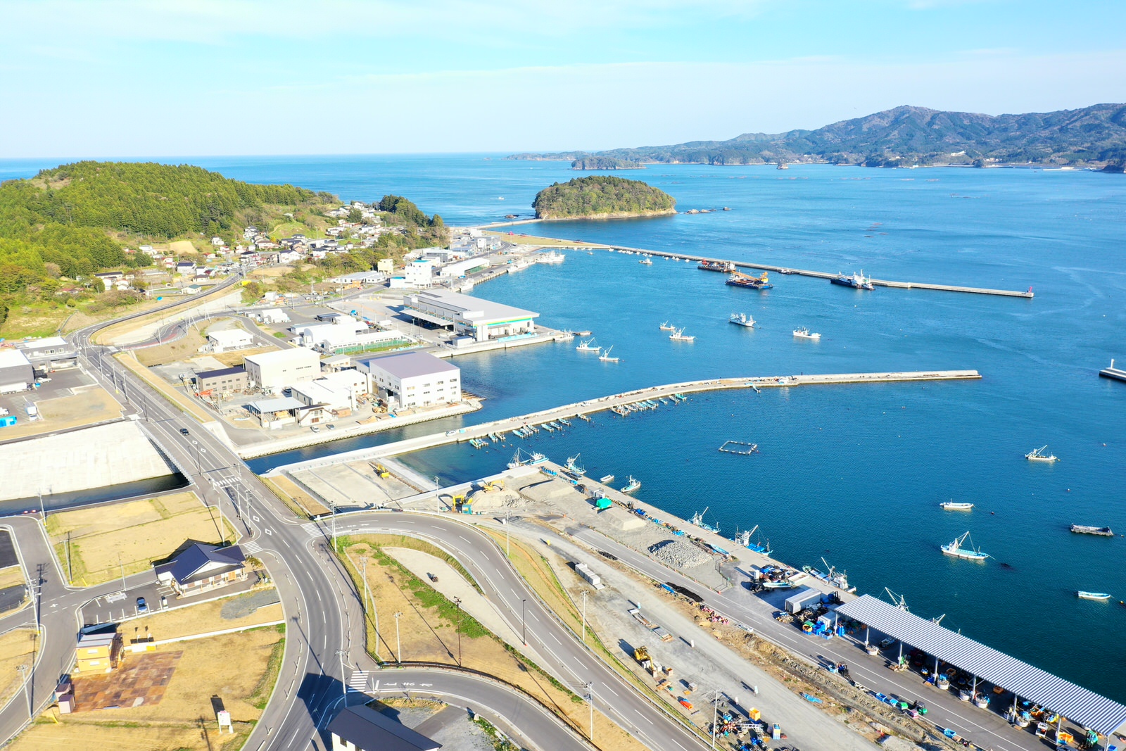 海沿いの町と港が広がり、建物や船、道路などが点在する様子を空から撮影した港町の写真