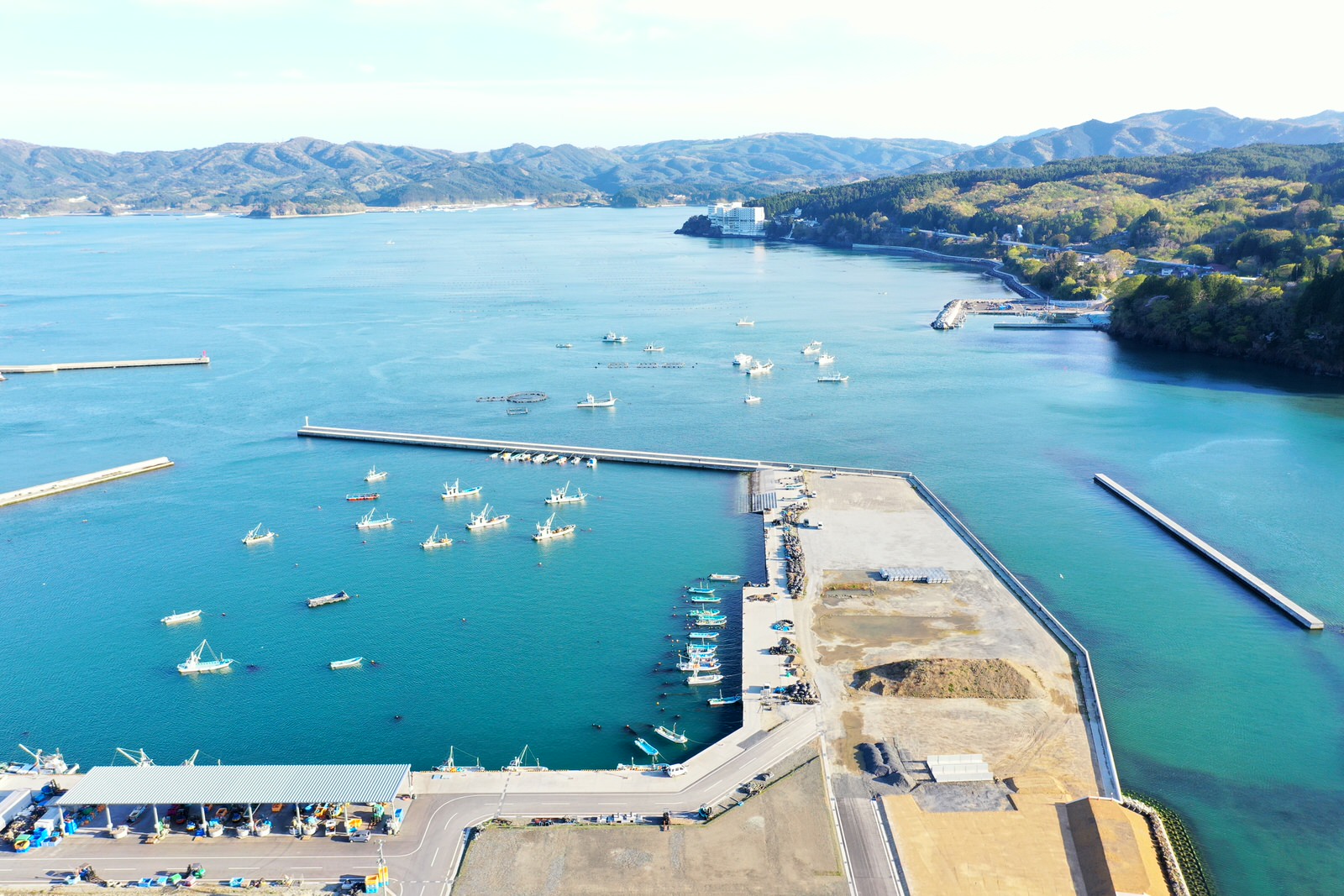 南三陸町の港を上空から撮影した写真で、湾の内側にたくさんの漁船が停泊しており、防波堤や岸壁の整備された港のまわりには山々と町の建物が広がっている様子を写した写真