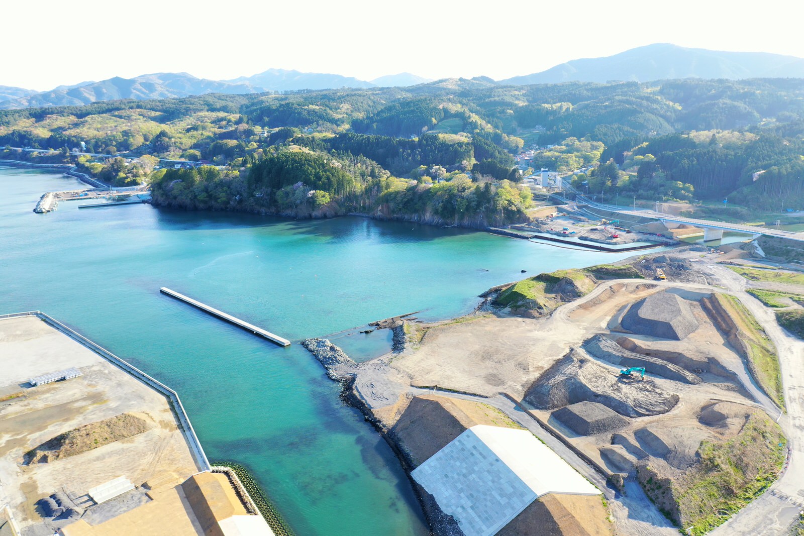 海に面した工事現場が広がり、その周囲には緑豊かな山々が連なっている様子を空から撮影した海辺の工事現場の写真