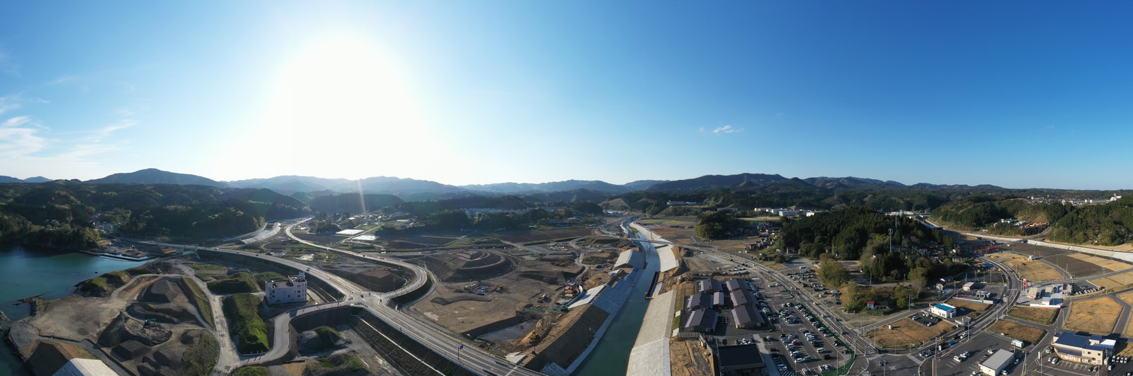 広大な土地に川が蛇行しながら流れ、その周囲には山々が連なり、建物や道路が点在する様子を空から撮影した山間の川と町の写真