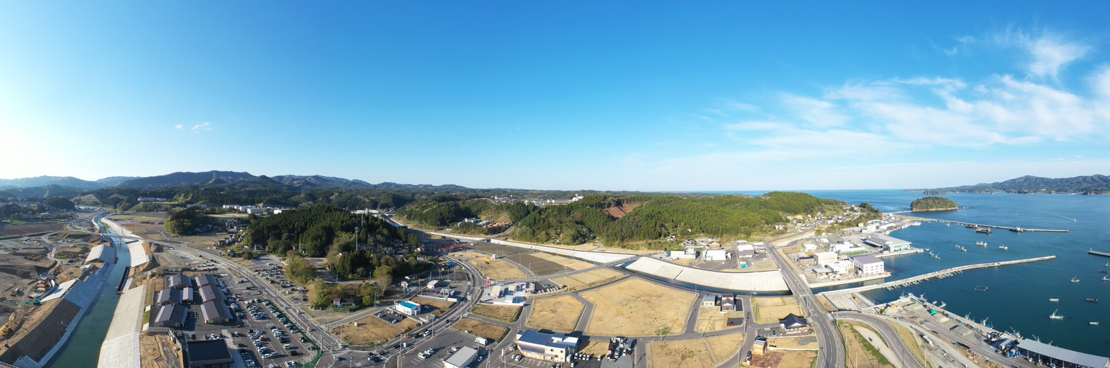 青空の下、海と山に囲まれた港町の全体が広がり、建物や港の様子が一望できる風景を空から撮影した港町の写真