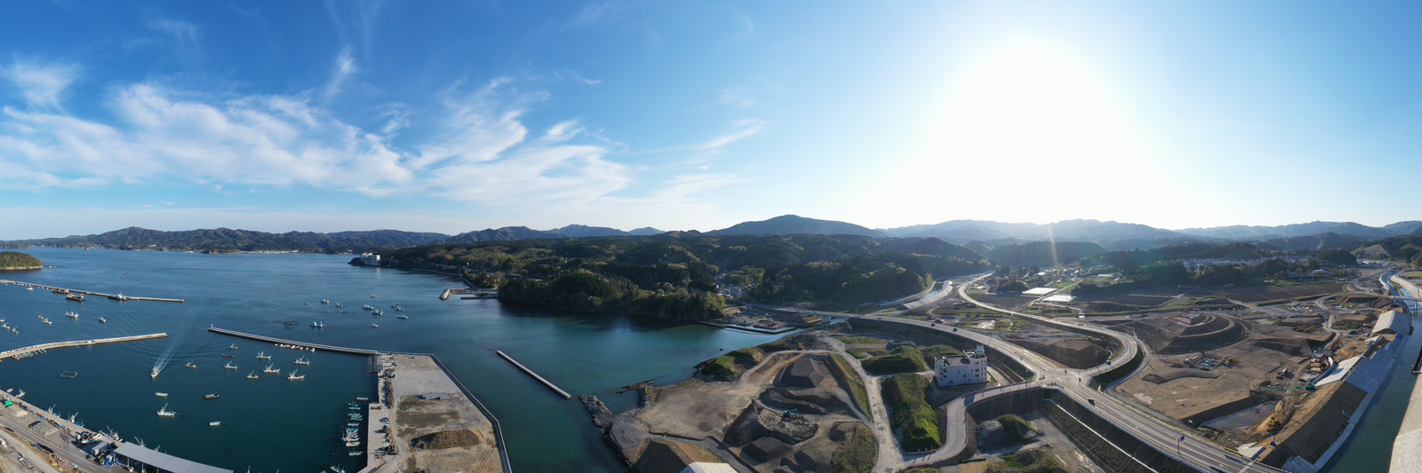 青い空の下、海に囲まれた港とその周辺に広がる建物や道路、船の様子を空から撮影した港の写真