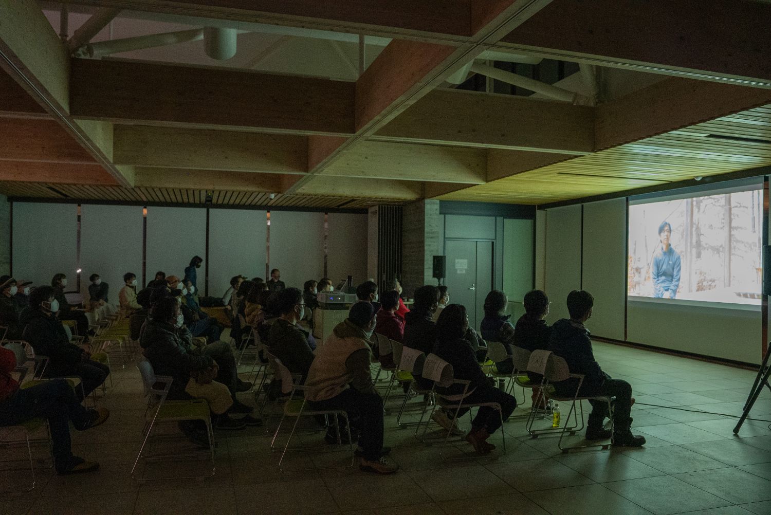照明を落とした木造天井の会場で、多くの来場者がスクリーンを静かに見つめながら着席しており、環境共生をテーマにしたパタゴニアのドキュメンタリーフィルム『共生のために走る』の上映が行われている様子の写真