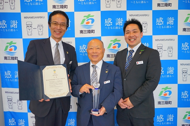 3人の男性が並んで立ち、それぞれが賞状やトロフィーを手にして表彰の場面にいる様子を写した写真