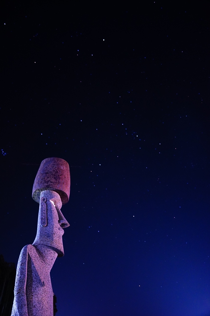 夜空の下にモアイ像が紫がかった照明でライトアップされている写真