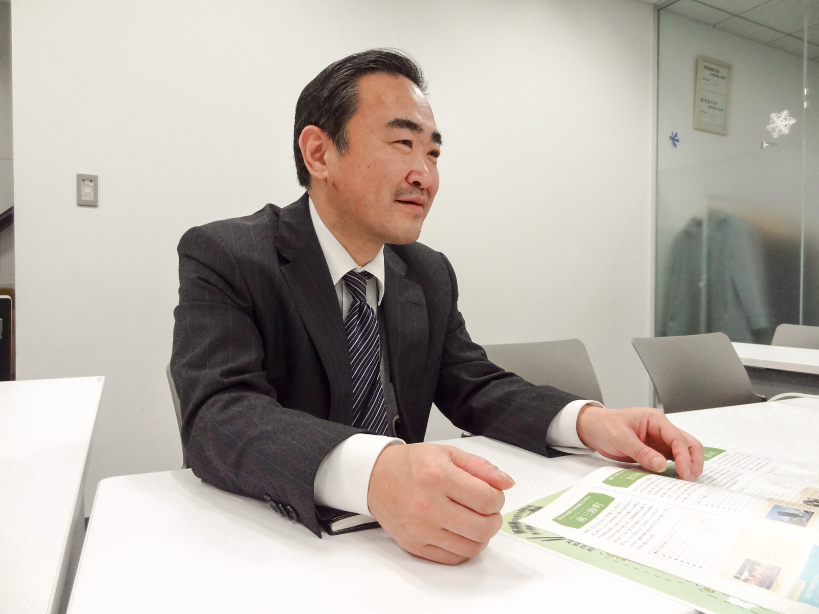 スーツを着た男性が白い会議机の上の資料を前に話をしている様子の写真