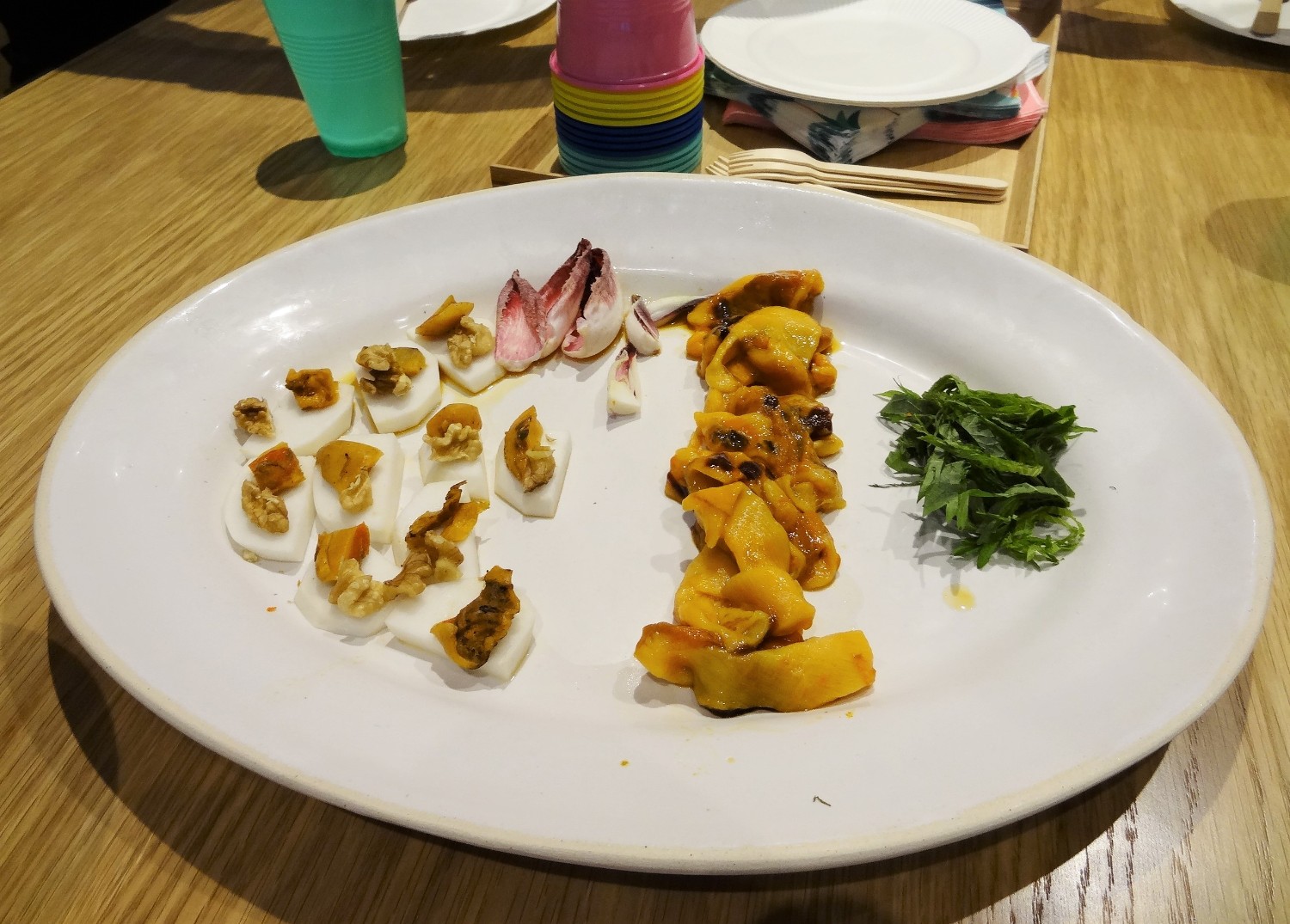 白い大皿に、燻製ホヤと茶色いクルミが乗った前菜と、ホヤの刺身、付け合わせの刻んだ大葉が盛られている写真