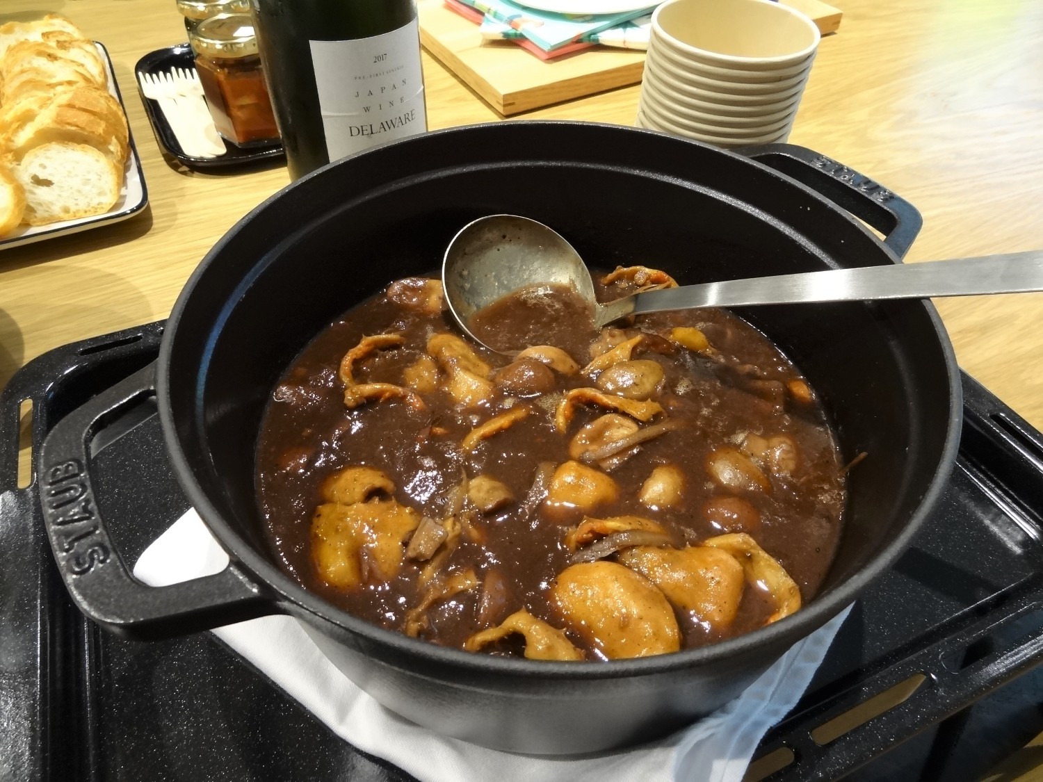 黒い鍋の中に、ホヤを赤ワインで煮た料理がたっぷりと入っており、隣にはスライスされたフランスパンが並べられている写真