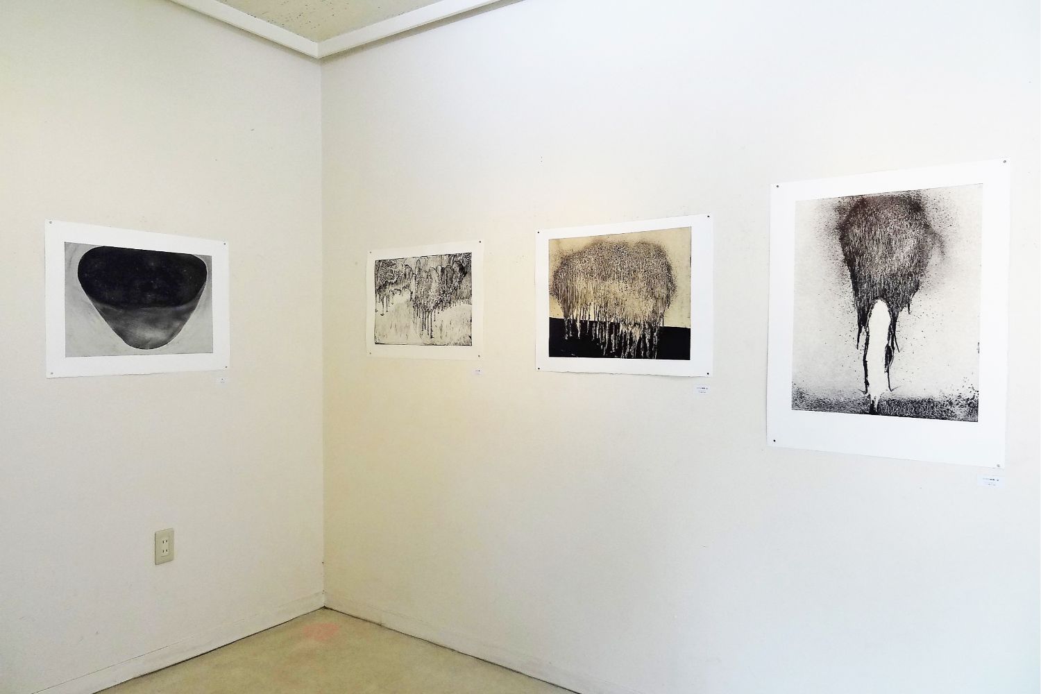 様々な質感や形が表現されている白と黒の抽象的な版画作品が4点、壁に展示されている画廊内の写真
