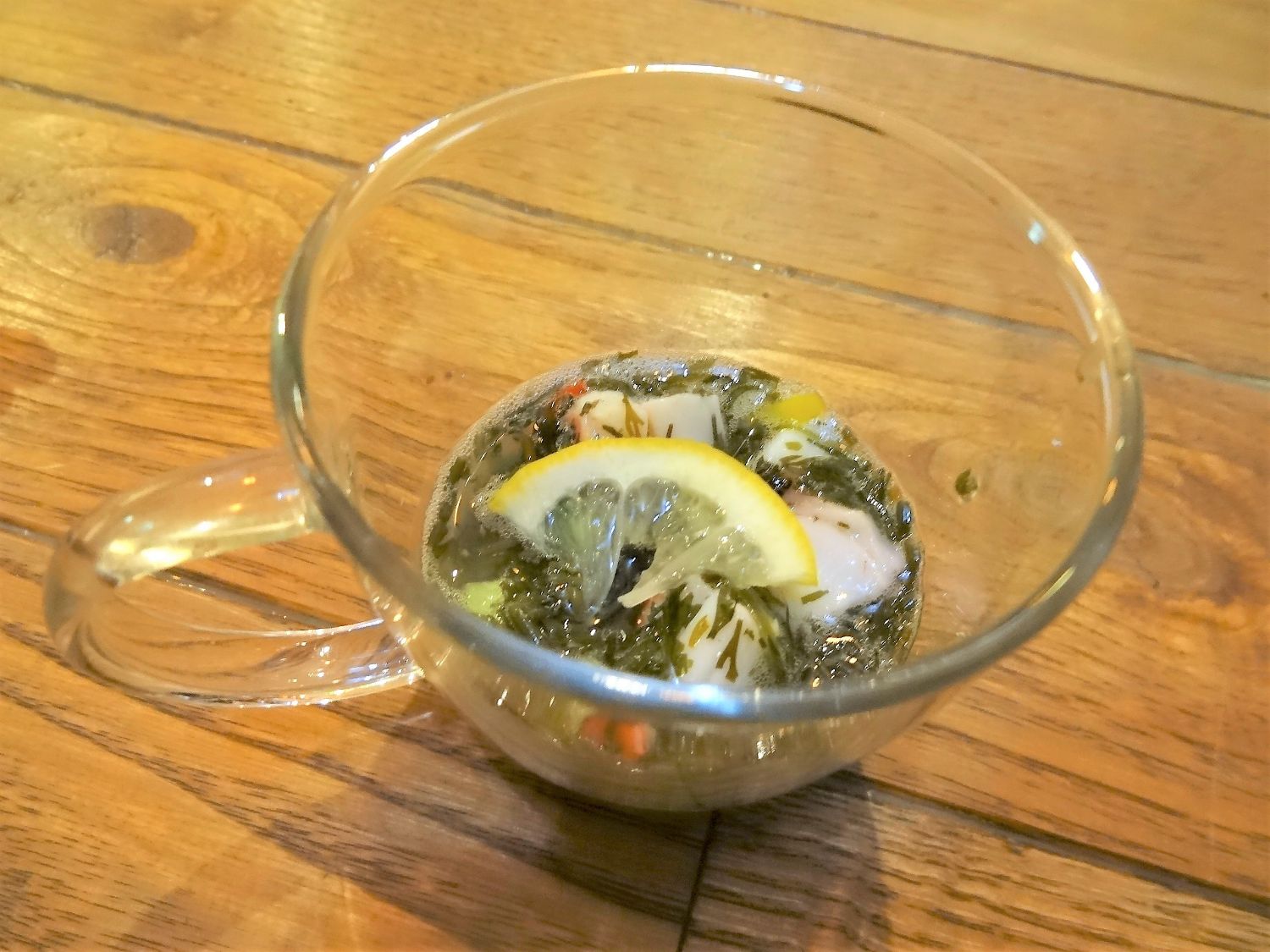 透明なガラスのカップにレモンと海藻、たこなどが入ったカクテルサラダの料理がテーブルの上に置かれている写真