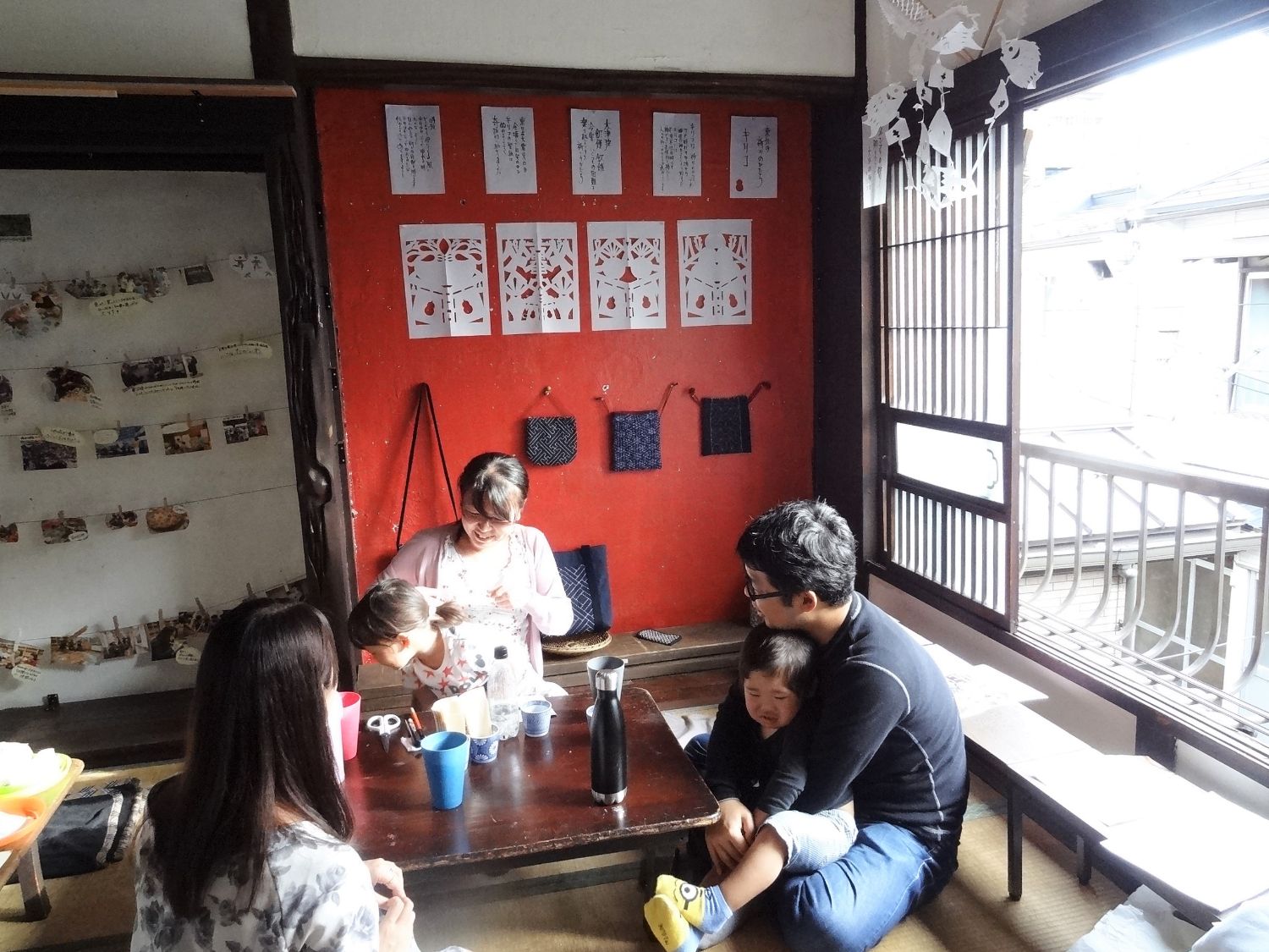 右側の大きな窓からは自然光が差し込んおり、和風の室内で家族や子どもたちがくつろいだり、遊んだりしている様子の写真