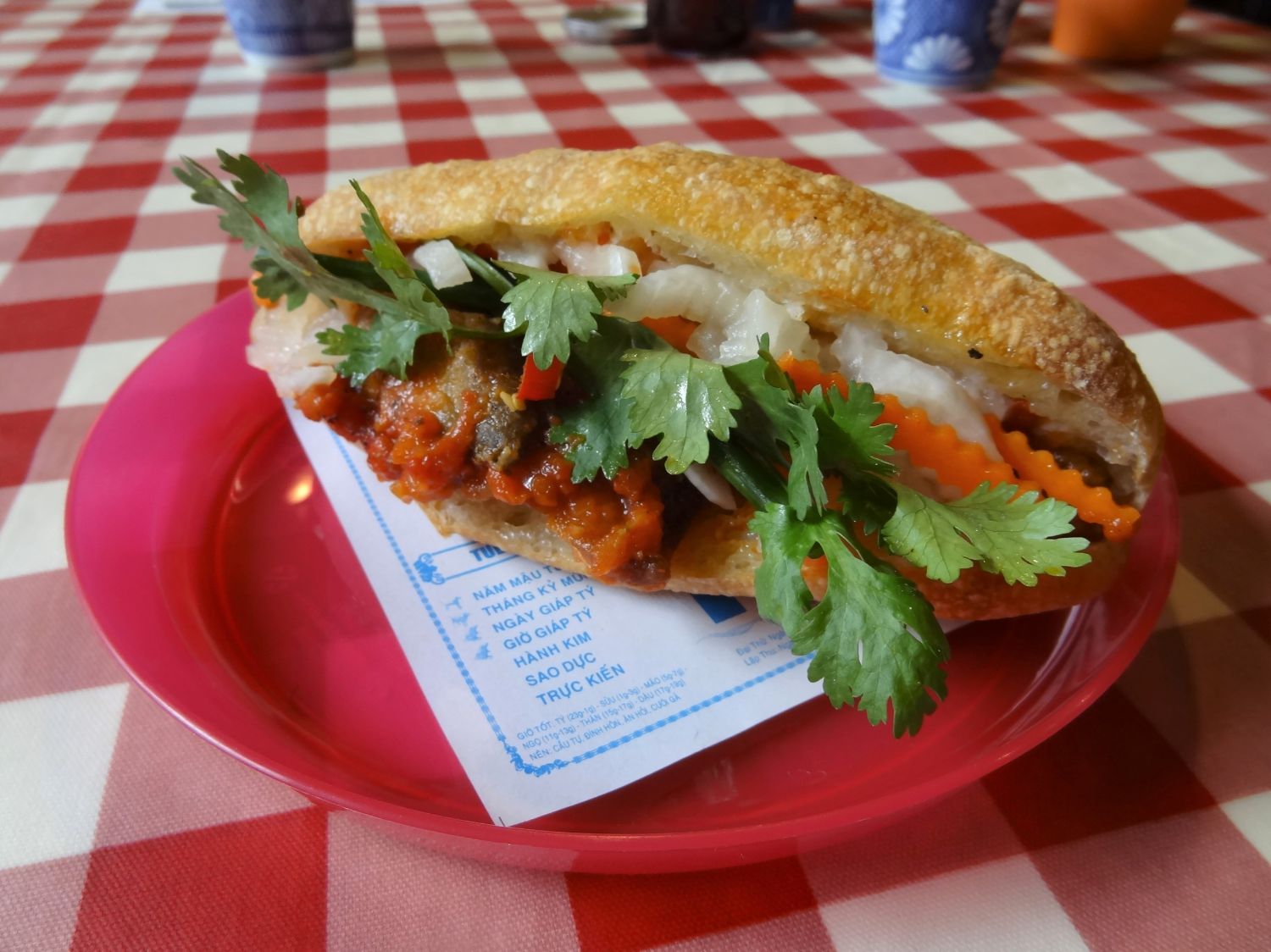 赤と白のチェック柄のテーブルクロスが敷かれ、お皿に盛られた鯖トマトソースのバインミーの写真