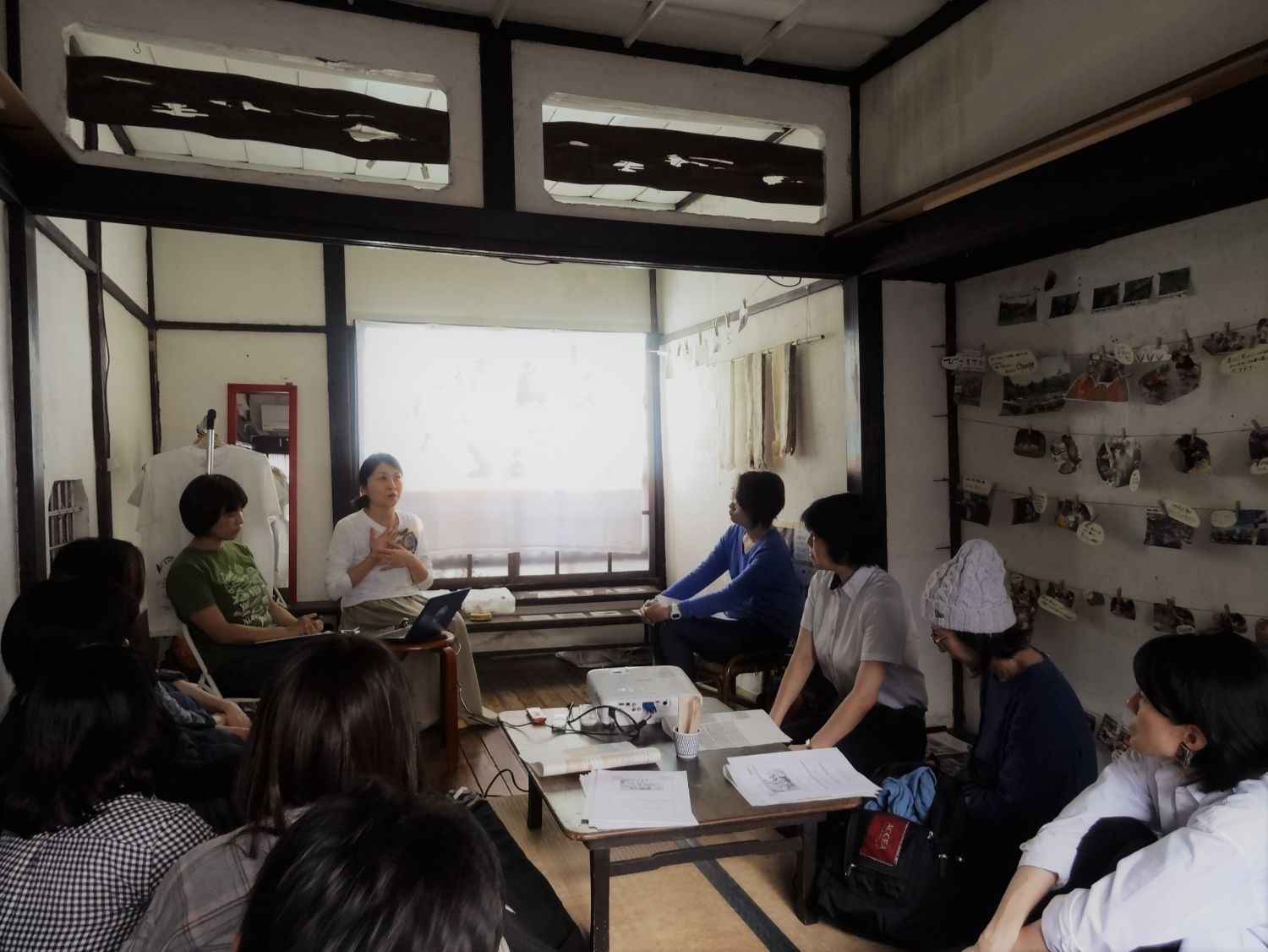 和風の古民家のような室内で白い服の女性が話しているのを参加者達が聞いているお話会の様子写真