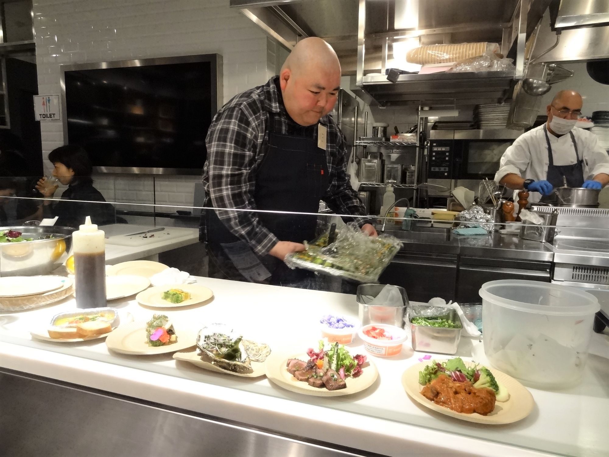 黒色のエプロンを着用した店長の新井さんがバットに入った材料を持って忙しそうに調理を行っている写真