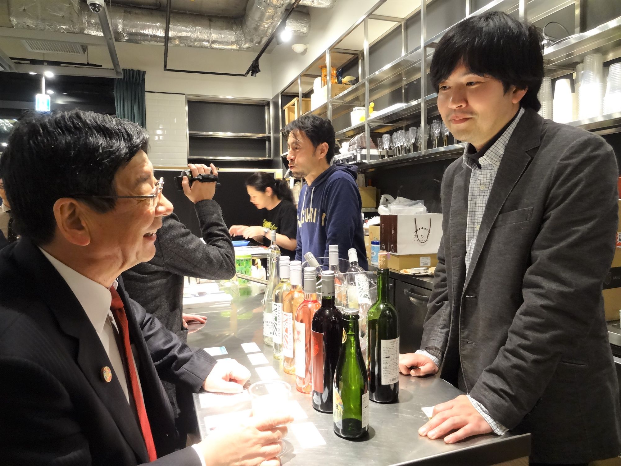 赤いネクタイをしめた佐藤仁町長と南三陸ワイナリーの正司さんが楽しそうに話をしている様子の写真