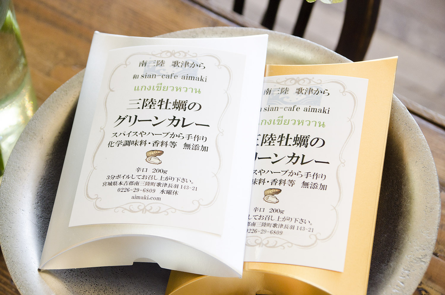 白とオレンジの箱に入った「三陸牡蠣のグリーンカレー」のパッケージが皿の上に並べられている写真