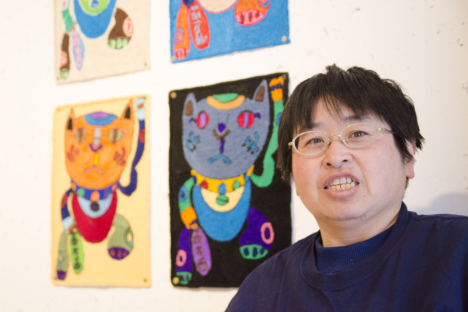 カラフルな猫の作品が壁に展示されている前で写っている前川さんの写真