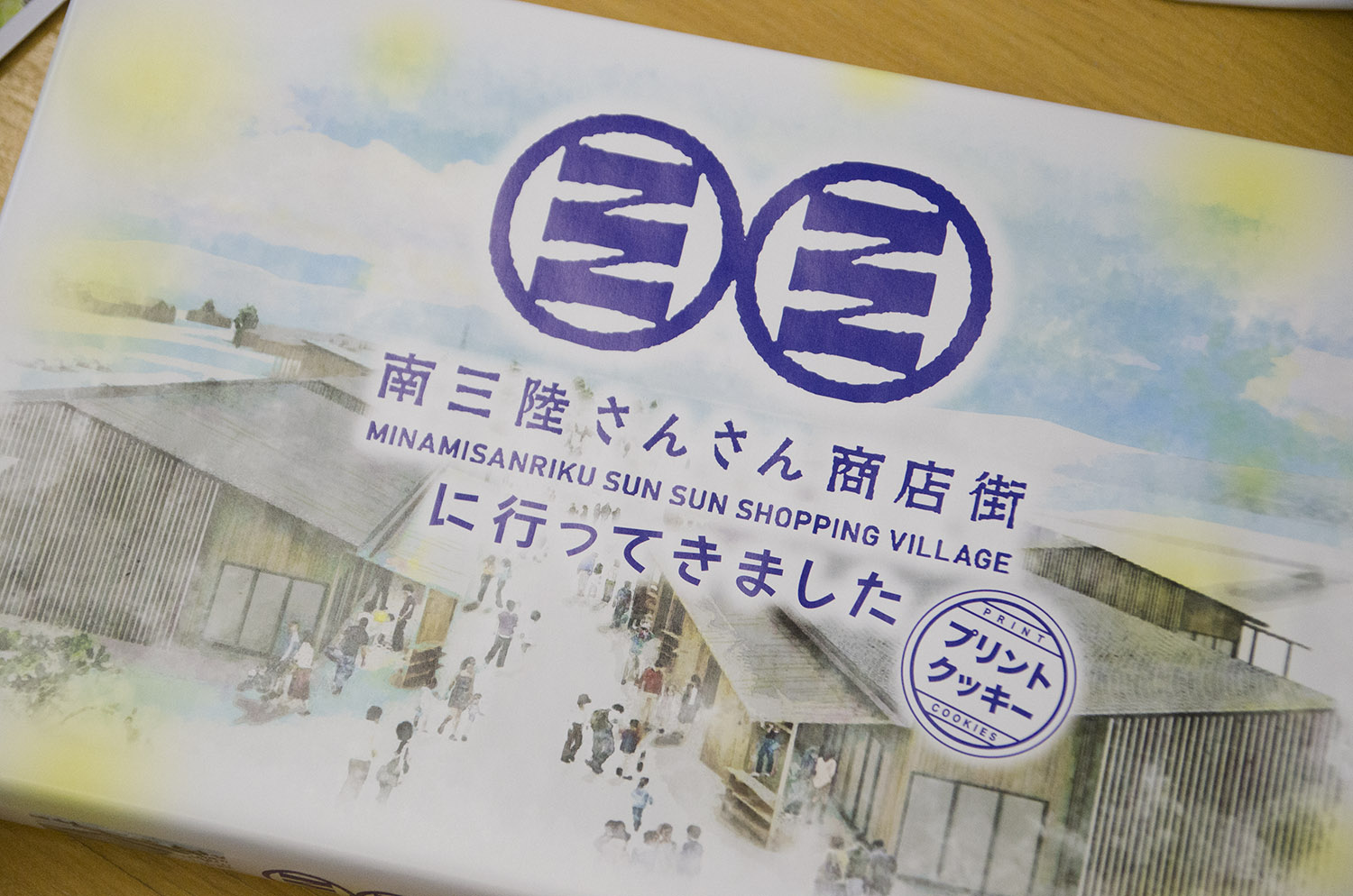 『南三陸さんさん商店街に行ってきました』と書かれた、商店街のイラストが描かれているプリントのクッキーのパッケージをアップで撮影した写真