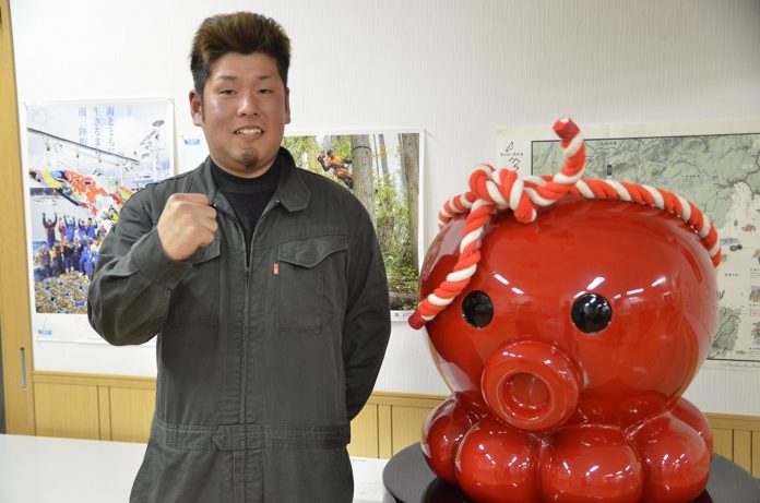 紅白のねじり鉢巻きを巻いた赤いタコのキャラクター「オクトパス君」の像の横に立った千葉さんがガッツポーズをしている写真