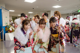 会場のロビーに2列に並んだ、華やかな花柄の着物と毛皮のショールを身にまとった7人の女性が、カメラに向かってピースサインをしている写真