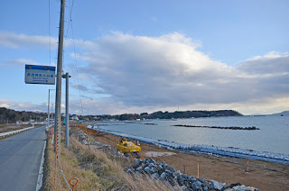 海岸の前を通る道路の脇の電柱に案内の看板が設置されており、海岸には重機が置かれている写真