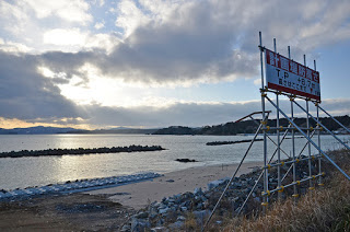 消波ブロックが並ぶ海岸の手前に「計画堤防高さ」と書かれた赤と白の配色の看板が設置されている写真