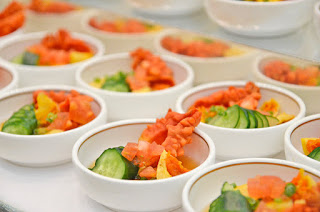 キュウリなどの野菜とオレンジ色の貝が盛り付けられた白い小さなお椀がたくさん並んでいる写真