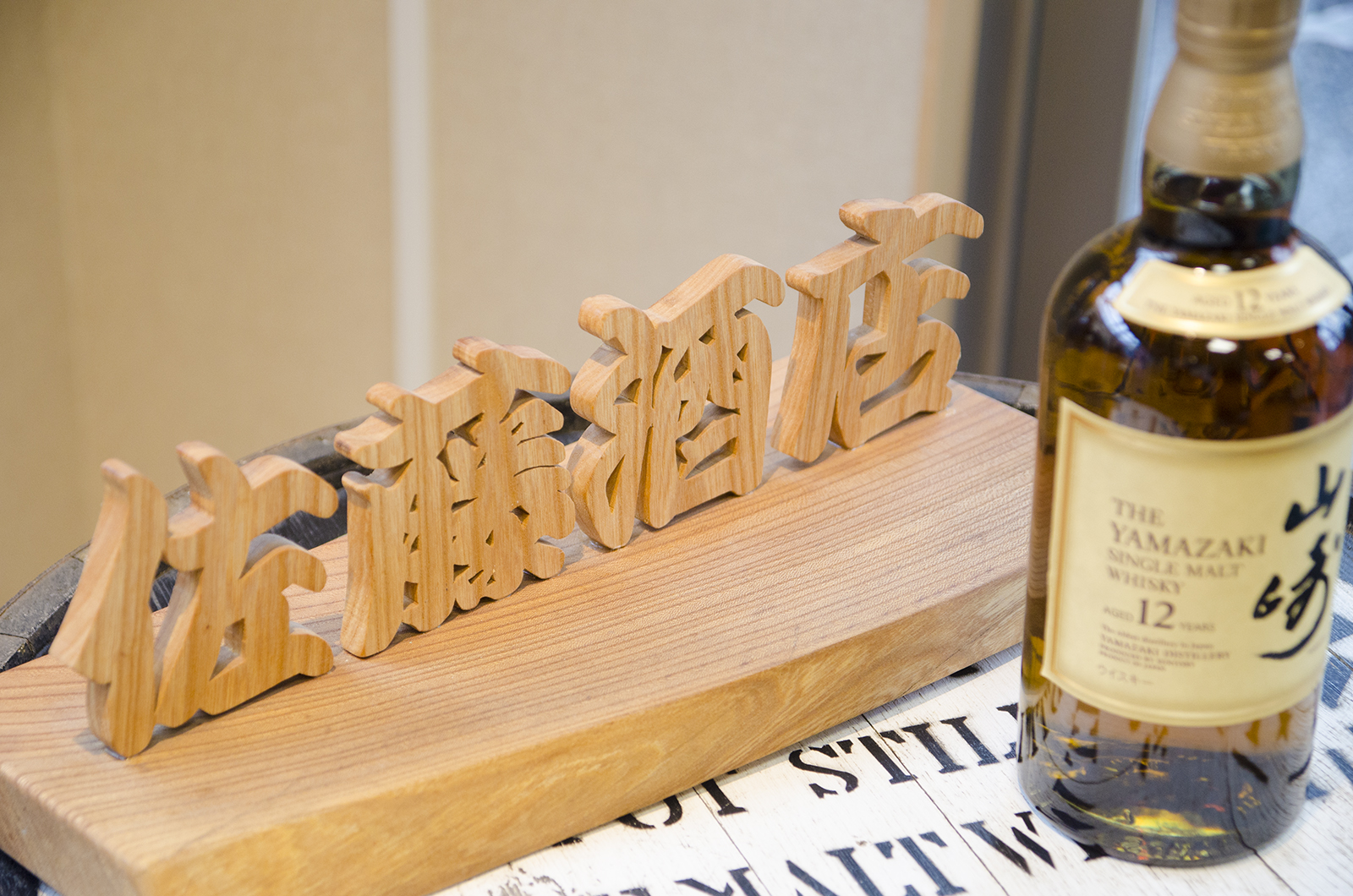 木で彫られた「佐藤酒店」の文字と「山崎」のラベルが貼られたウイスキーの瓶が並べて置かれている写真