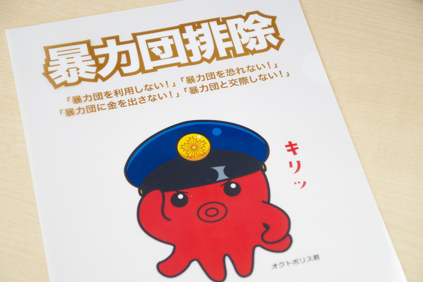 「暴力団排除」の大きな文字の下に、「暴力団を利用しない！」「暴力団を恐れない！」「暴力団に金を出さない！」「暴力団と交際しない！」の文字と警察帽をかぶり、きりっとした表情で敬礼をしている赤いタコのキャラクター、オクトポリスくんが描かれているチラシの写真