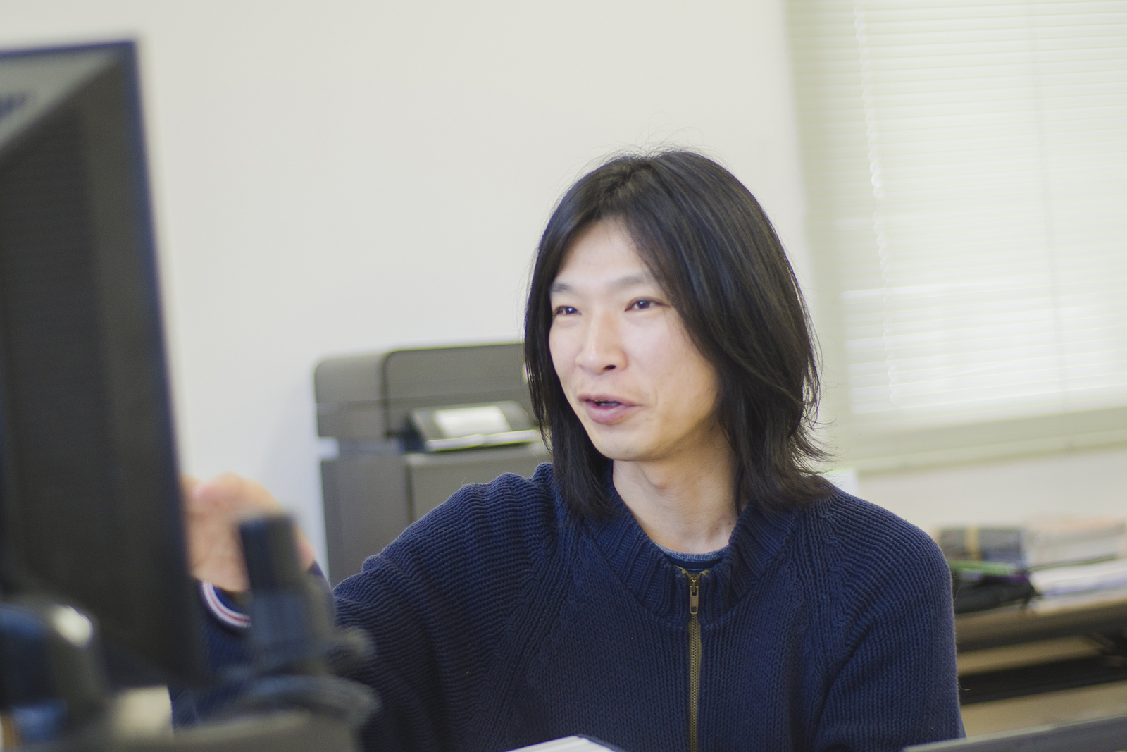 黒いモニターの前に座り話をしている佐藤さんの写真