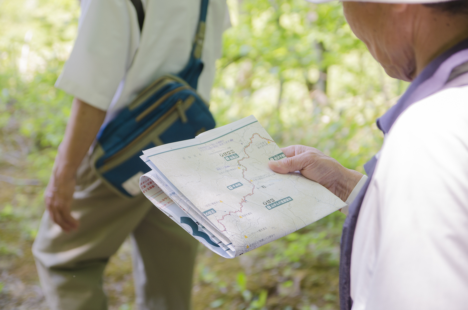 緑の木々の中を歩きながら、折りたたんだ地図を見ている参加者の写真