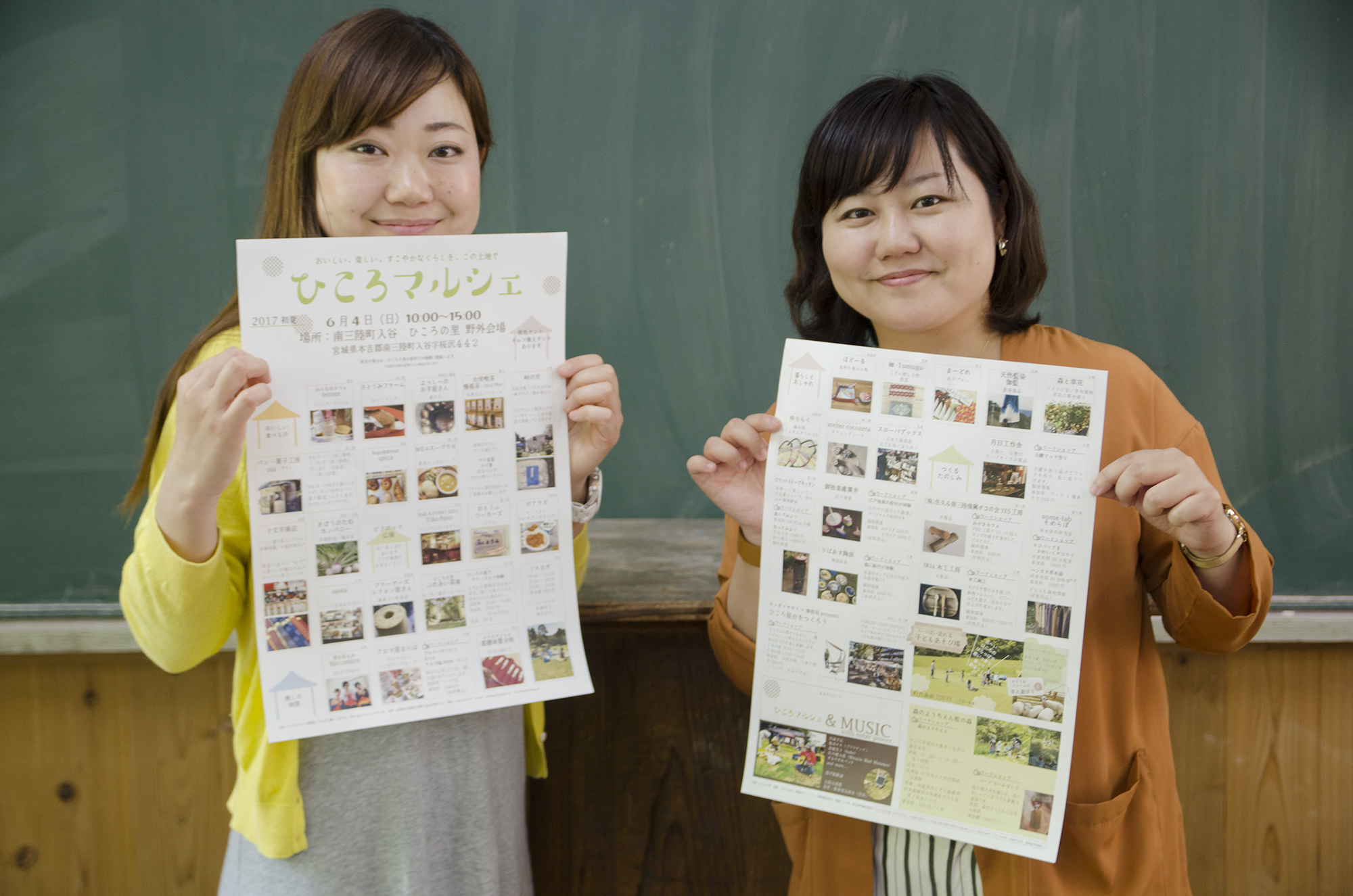 黒板が設置された壁の前で、ひころマルシェのチラシを持った中島さんと女性リポーターが並んで立っている写真
