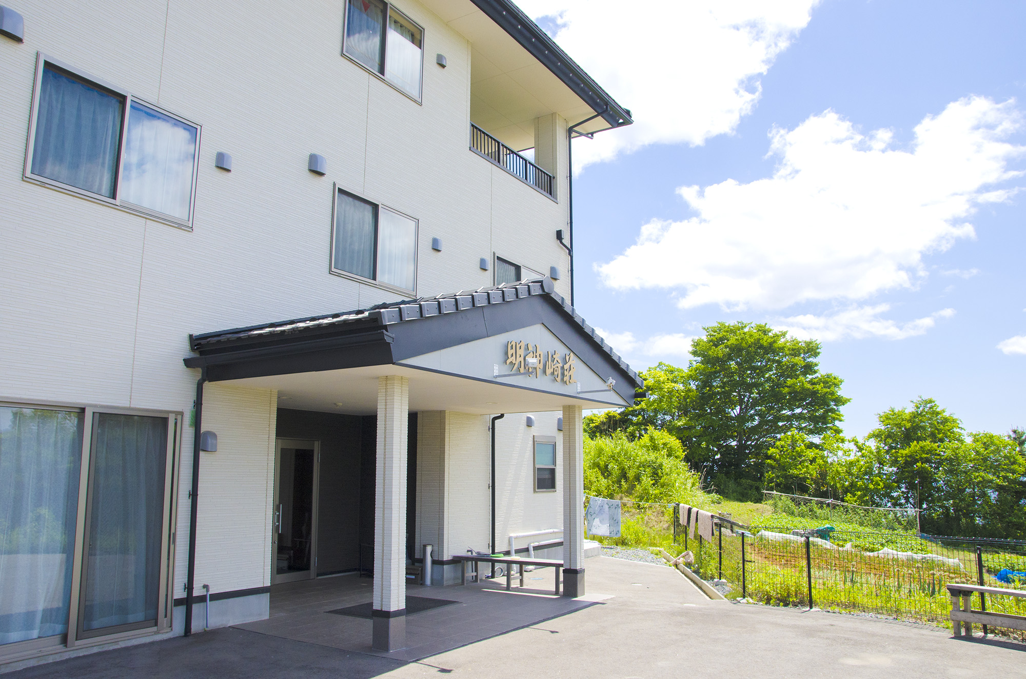 三角屋根の入り口部分に「明神崎荘」と書かれている、白い外壁で2階建ての明神崎荘の外観を写した写真