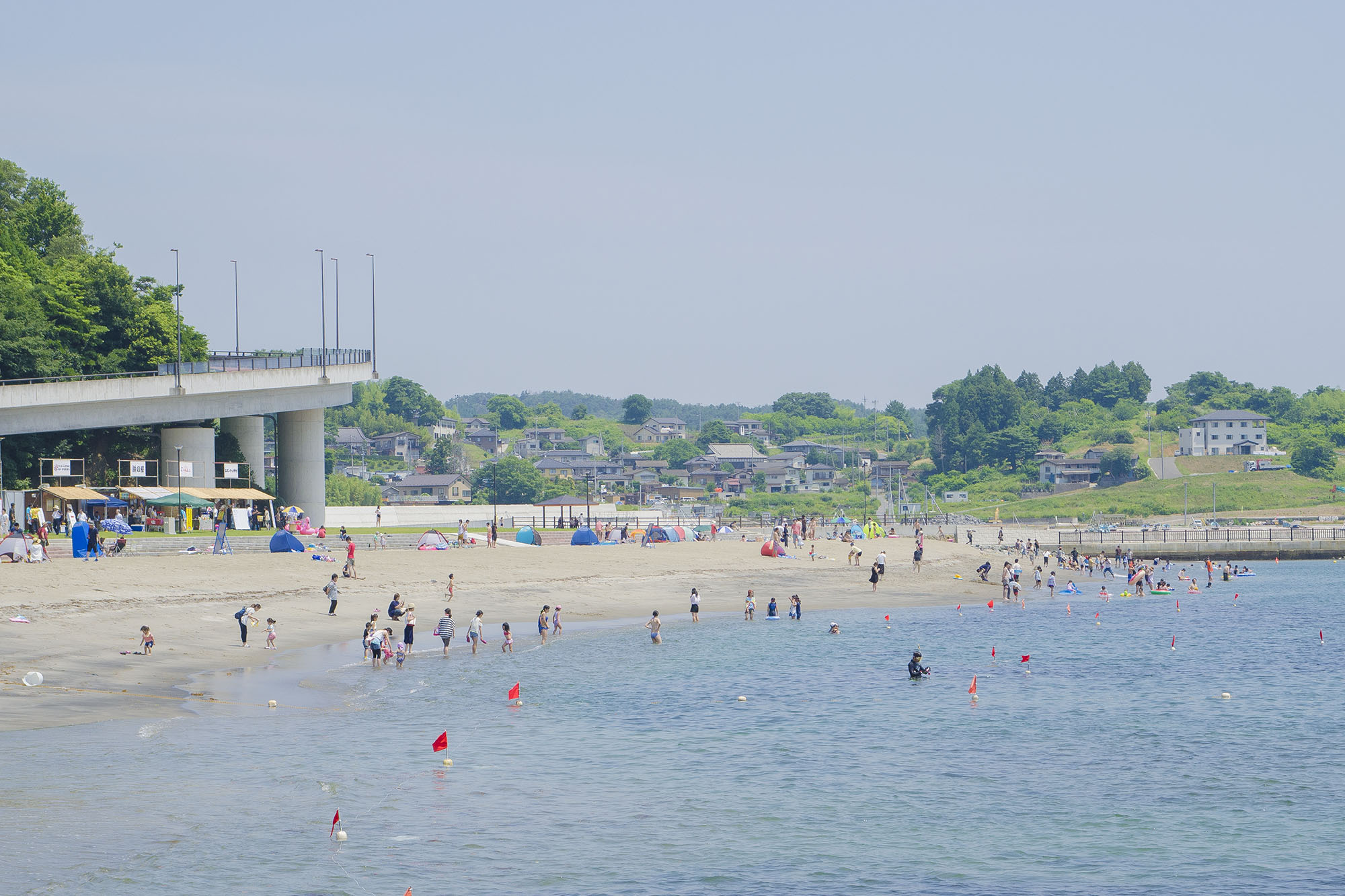 海岸沿いの広い砂浜で多くの人々が水遊びや散策を楽しんでいるのを遠くから全体的に写した写真