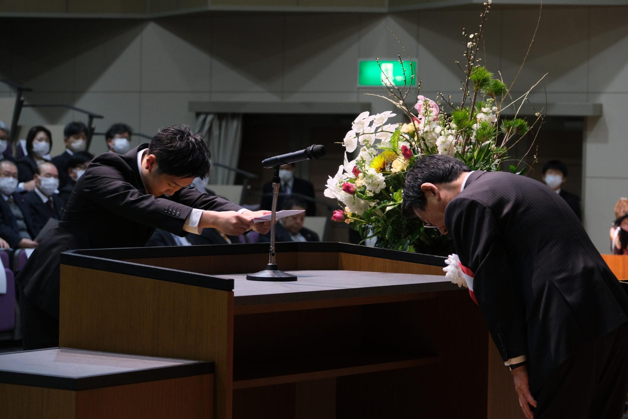 スーツ姿の新成人の男性と町長が演台前で互いに深く頭を下げ合っている写真