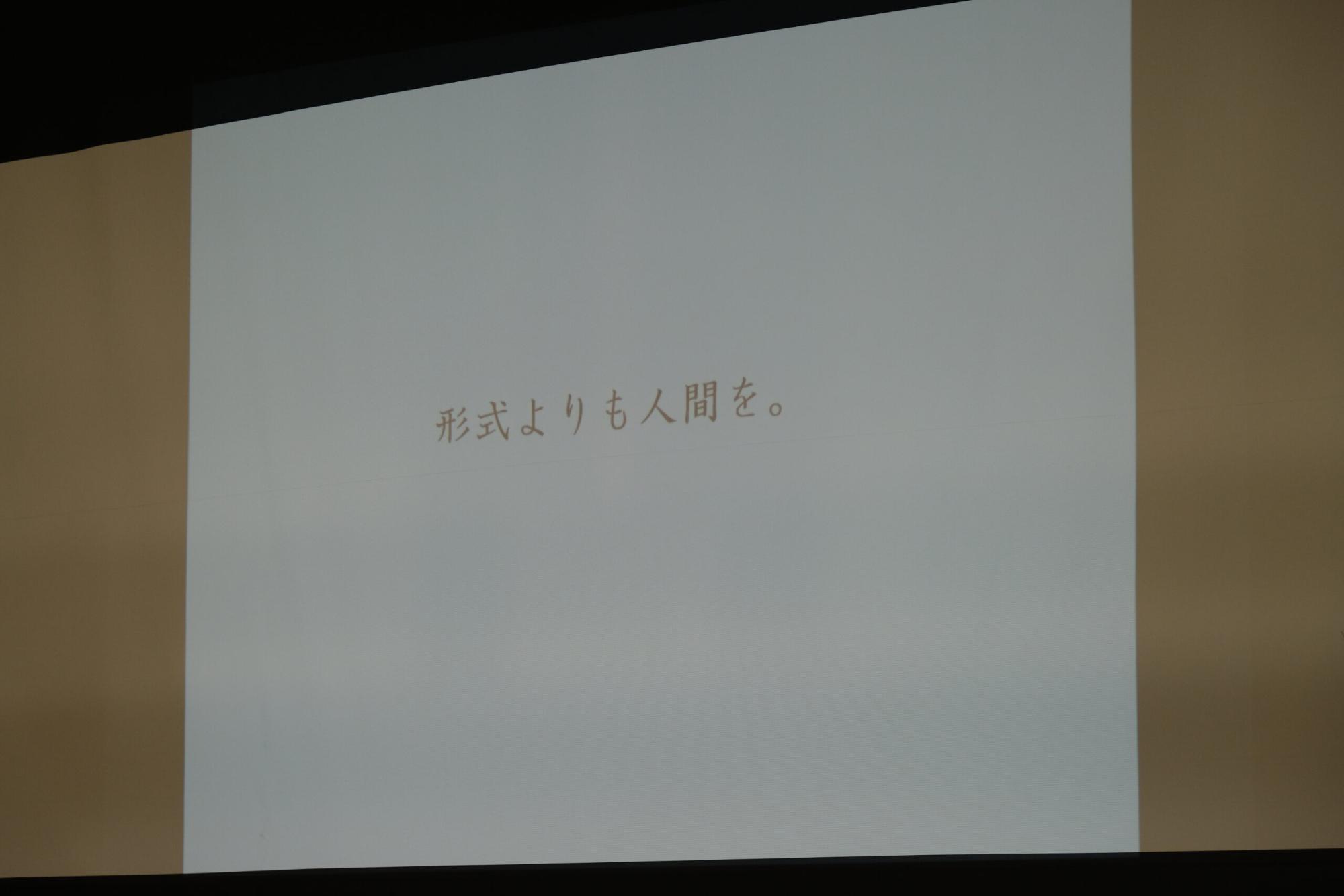 スクリーンに「形式よりも人間を。」というメッセージがシンプルに映し出されている写真