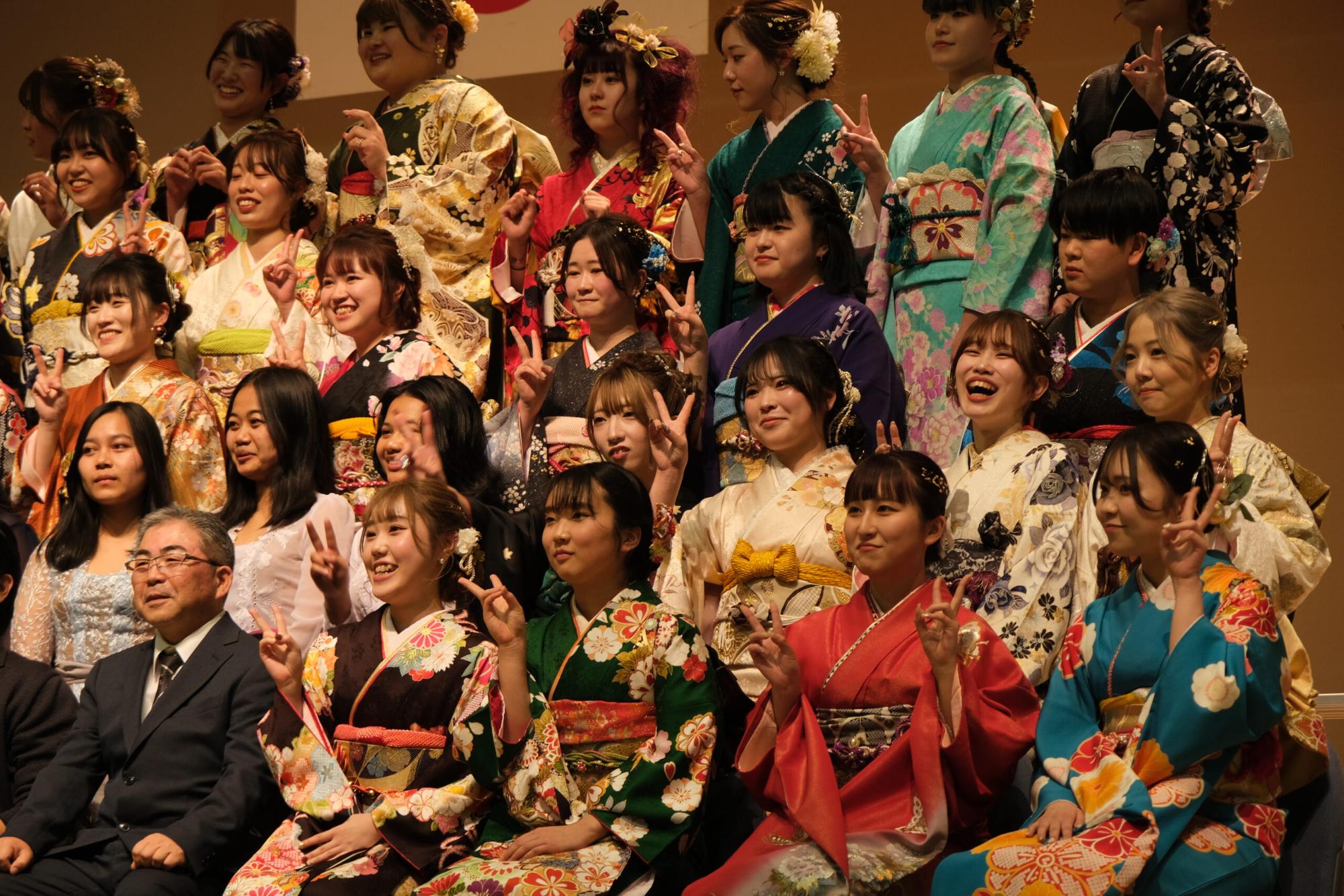 色とりどりの振袖を着た新成人女性たちが笑顔でピースサインをしながらカメラに向かっている、成人式後の記念写真