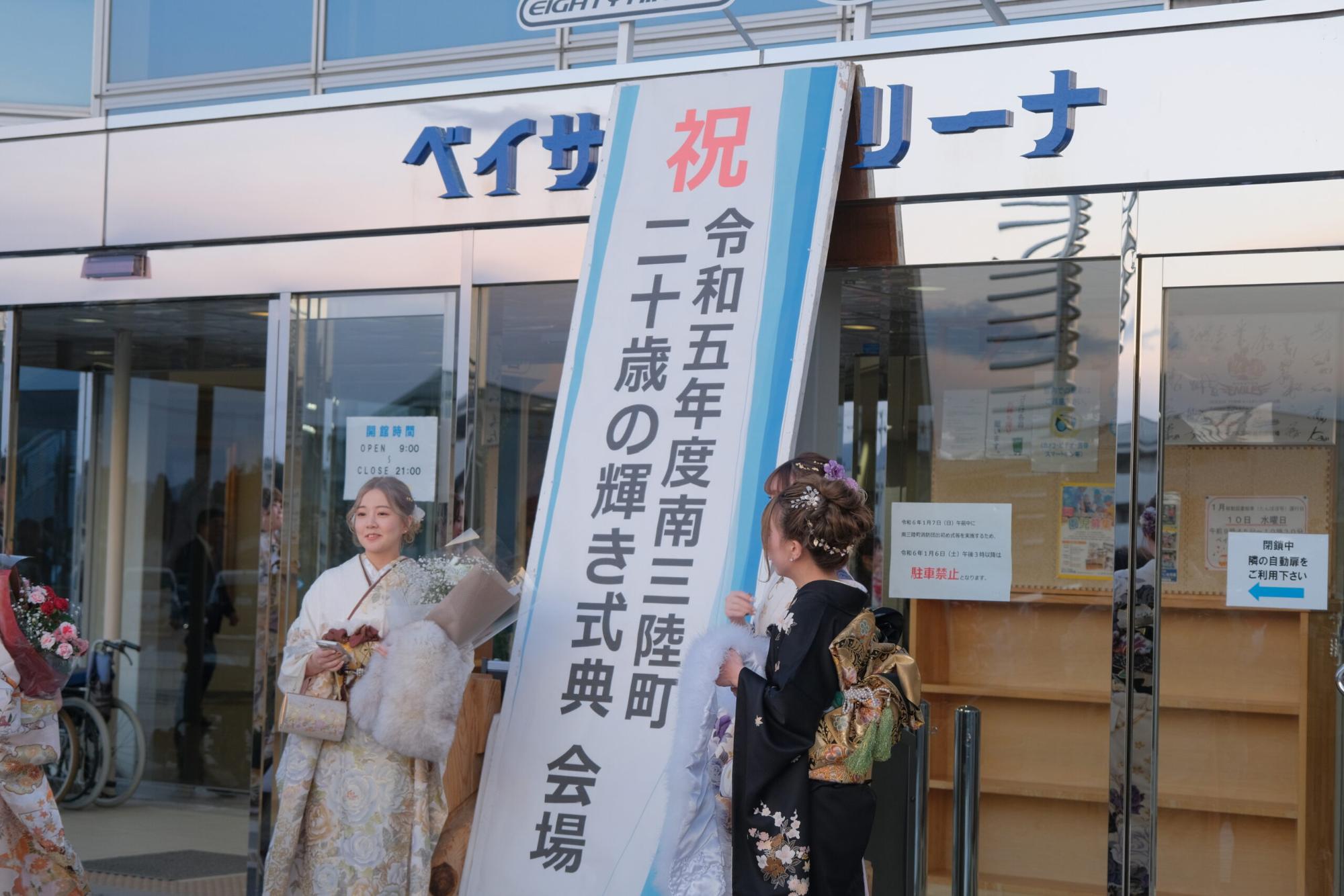 「令和五年度南三陸町二十歳の輝き式典会場」と書かれた立て看板の前で、振袖姿の新成人女性たちが記念撮影をしている、式典会場入口での記念写真