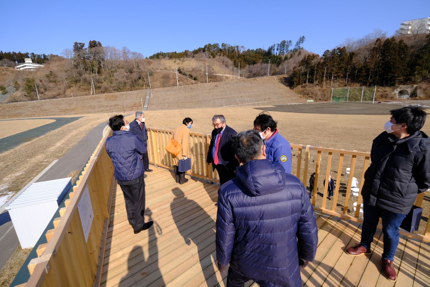 晴天の屋外で、両側に柵が設置された展望台の上で数名の人が見学している様子の写真