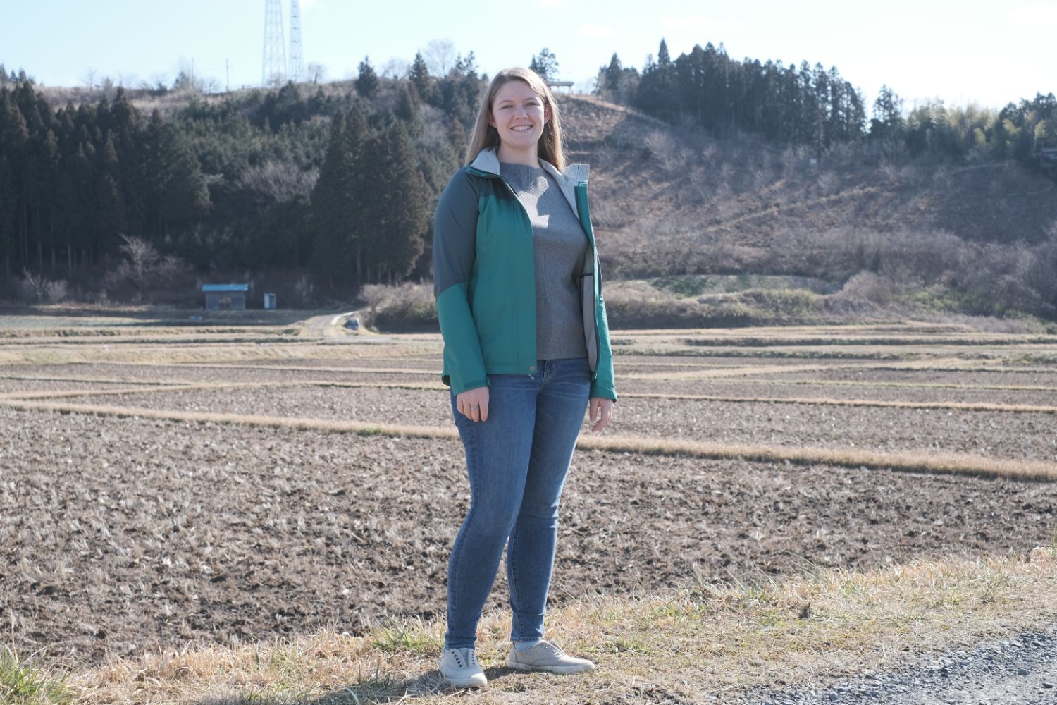 広々とした農地に笑顔で立つ、緑色のジャケットを着たケーリー・ワードさんをアップで撮影した写真