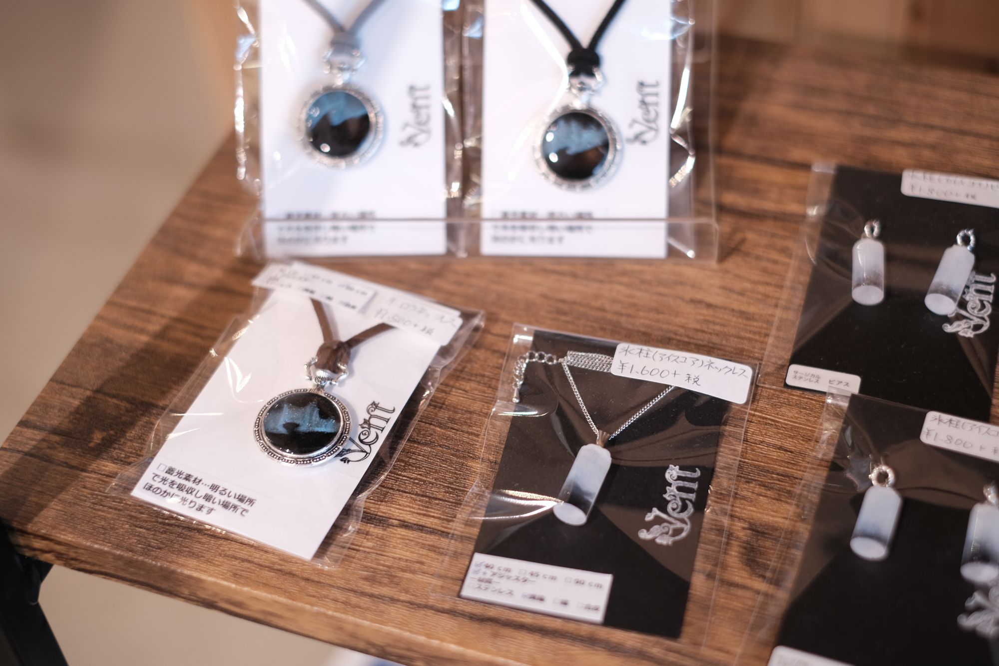 木製の台の上に、透明な袋に入れられた青や黒の円形デザインや半透明の長方形のネックレス4点とアクセサリー2点が並べられた写真