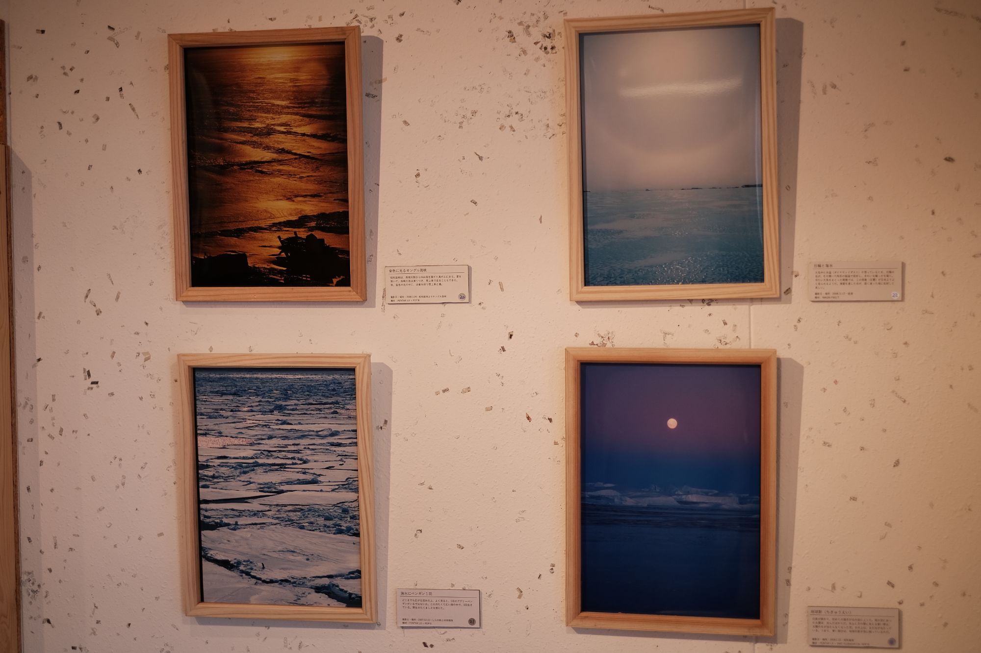 壁に飾られた4枚の額入り写真には、水辺や流氷の風景がそれぞれ異なる色調で写されており、夕焼けの水面、青みがかった静かな氷原、砕けた流氷が広がる地形、そして月が浮かぶ海のような景色が並ぶ自然風景の写真