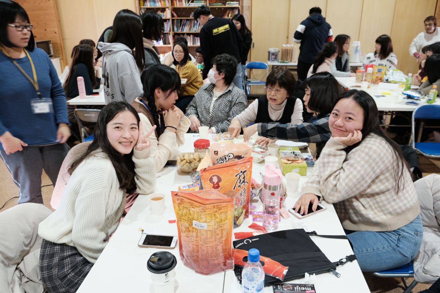お菓子が入った大きな袋や箱が置かれたテーブルの周りに台湾の女子大生や日本人の女性が座ってお菓子を食べている写真