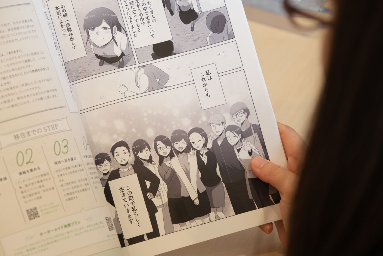 女性が移住ガイド冊子を手に取り、町での暮らしに希望を持つ若者たちが笑顔で肩を組みながら並び、『この町で私らしく生きていきます』というメッセージが添えられた漫画のページを読んでいる写真