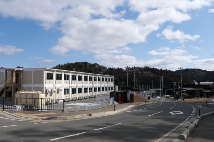 周囲には木が茂った山や見え、道路沿いに建っている真新しい2階建ての白い学生寮の写真