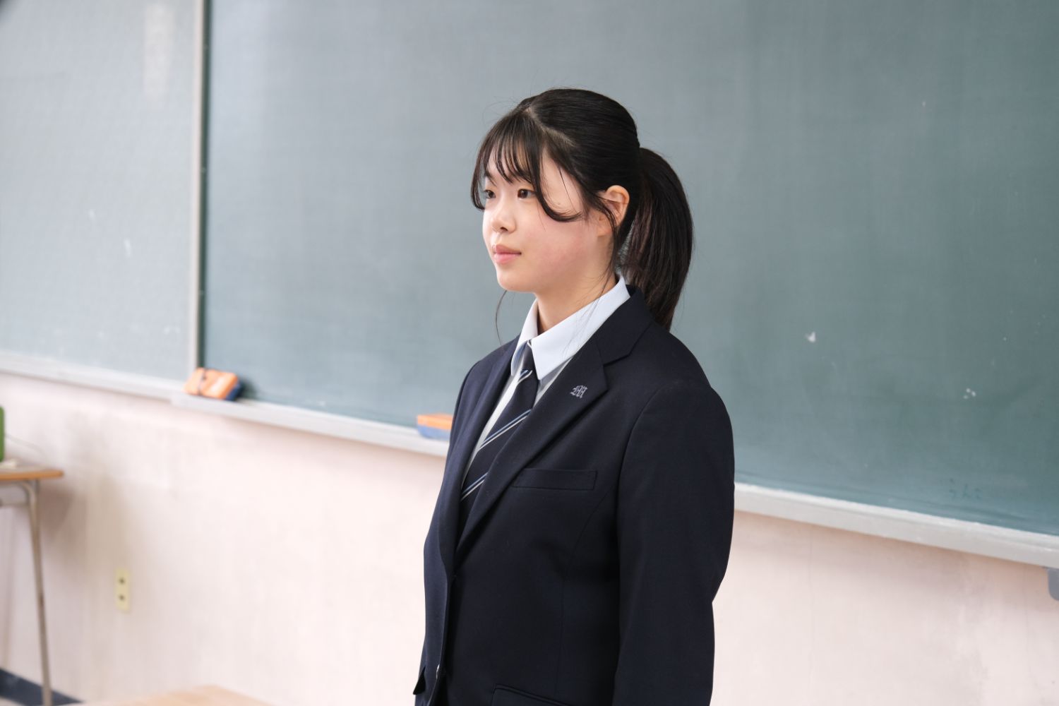 制服を着た伊藤さんが黒板の前でスピーチをしている写真