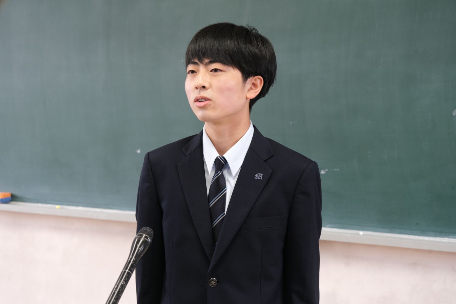 制服を着た小畑孝太朗さんが黒板の前でスピーチをしている写真