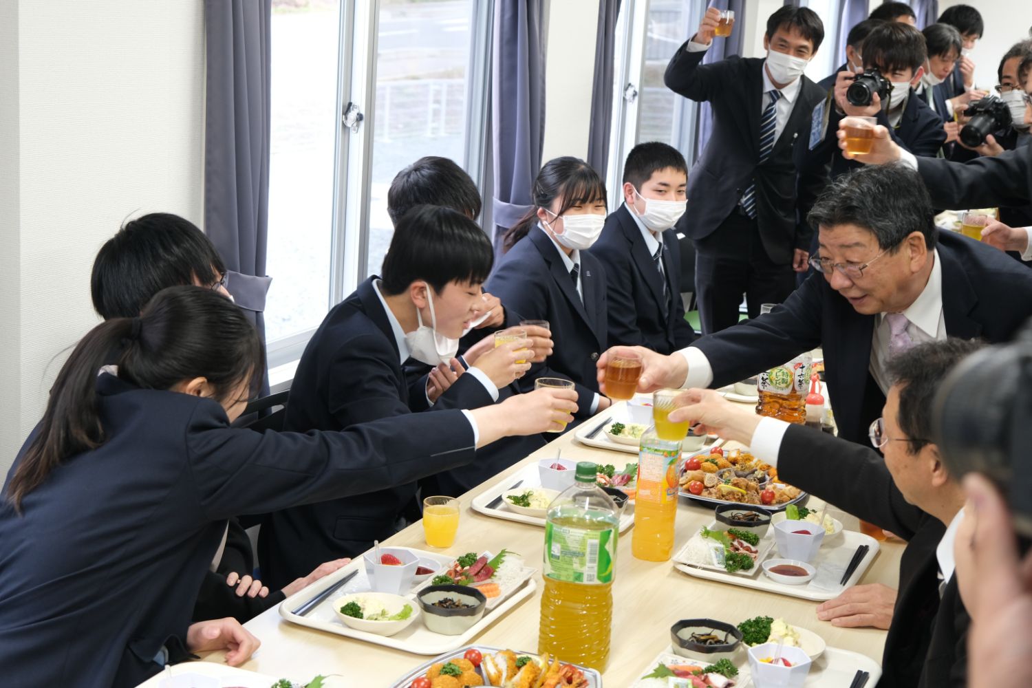 料理や飲み物が並んだテーブルを囲んだ入寮生たちと町長がが和やかに乾杯を交わす懇親会の様子の写真