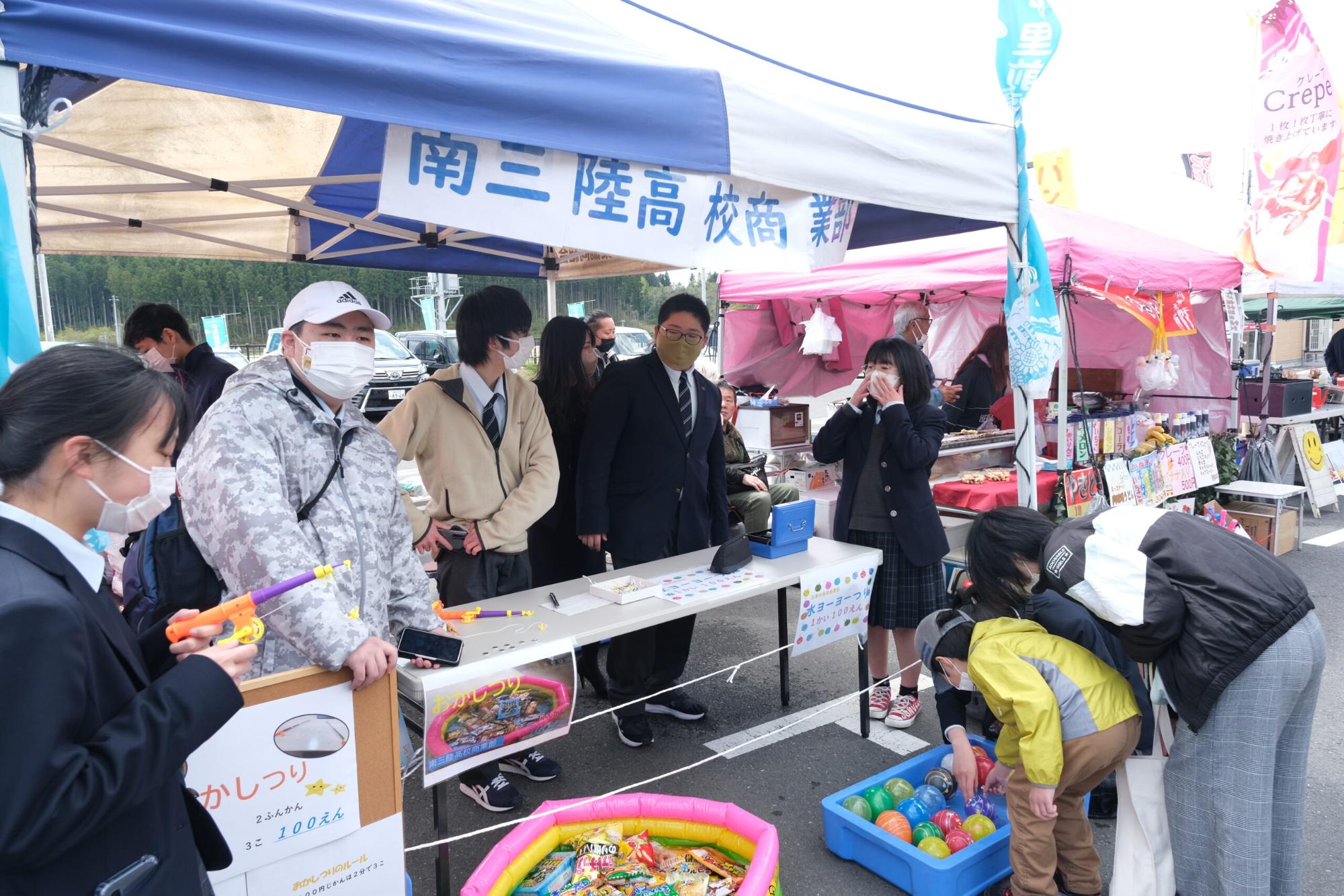 テントの下で高校生たちが屋台を運営しており、子どもたちがヨーヨー釣りを楽しんでいる写真